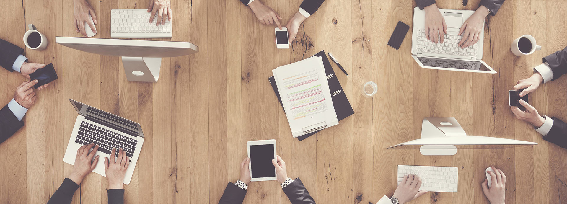 Ein gro&szlig;er Arbeitstiscg, auf dem acht Menschen an ihren elektronischen Ger&auml;ten arbeiten.