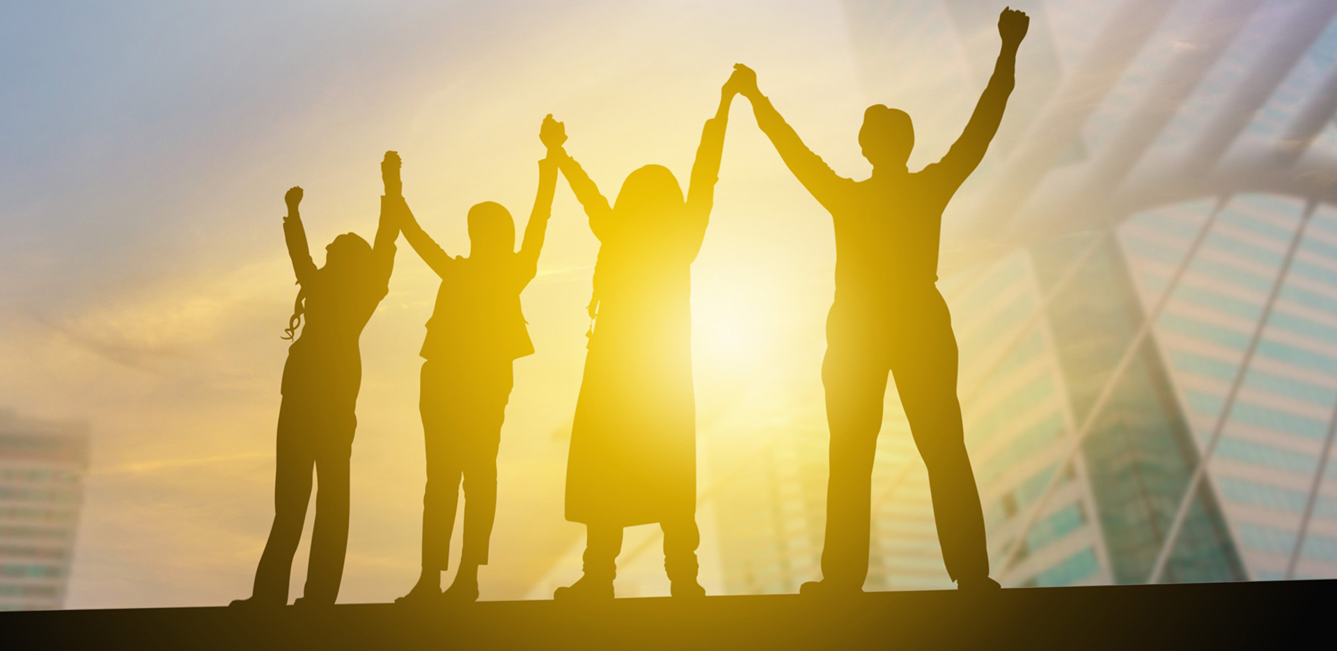 Vier Personen halten sich an den H&auml;nden und strecken ihre Arme in die Luft.